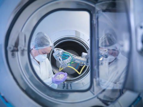 Worker inspects tablets in coating machine in pharmaceutical factory